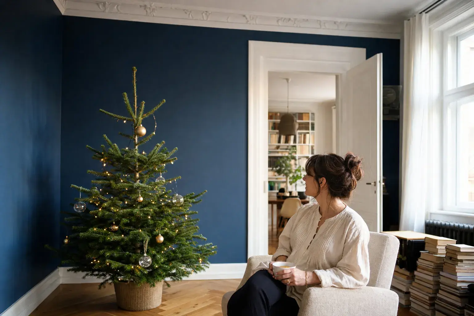 Tintenblau gestrichene Wand hinter einem geschmückten Weihnachtsbaum, daneben eine Frau im Sessel